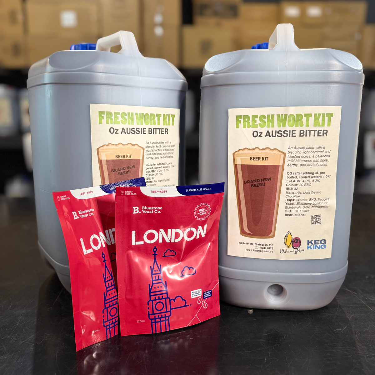 Two large gray containers labeled 'Fresh Wort Kit' and two red packets with 'London' branding on a dark surface.
